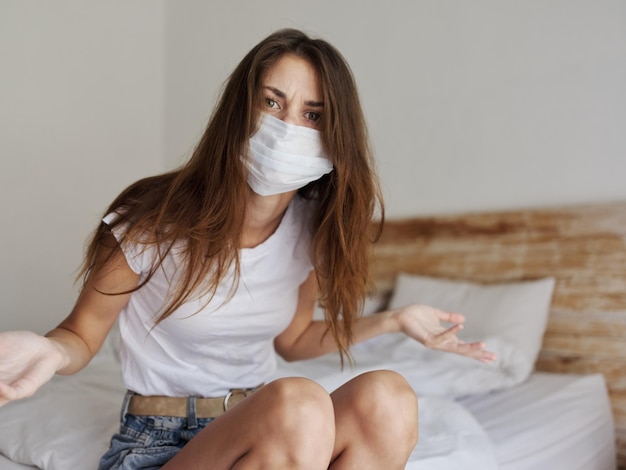 Une femme de remboursement portant un masque médical est assise sur la chambre à coucher et fait des gestes avec ses mains