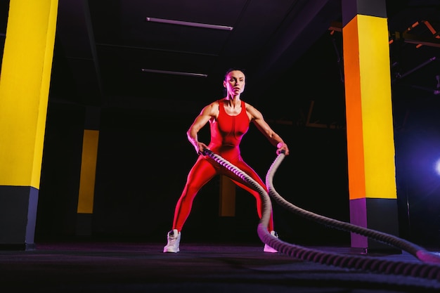 Femme de remise en forme à l'aide de cordes d'entraînement pour l'exercice au gymnase. Athlète travaillant avec des cordes de bataille au cross gym