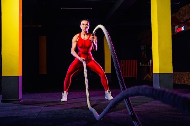 Femme de remise en forme à l'aide de cordes d'entraînement pour faire de l'exercice au gymnase. Athlète travaillant avec des cordes de combat au cross gym.