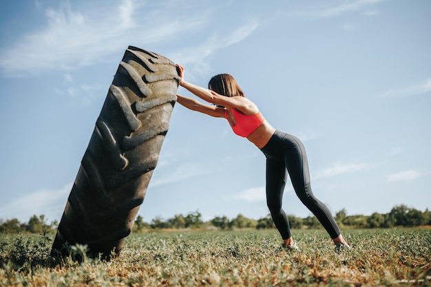 Femme de remise en forme dans la formation cross fit soulevant une roue dans le cadre de sa routine d'exercice cross fit traini