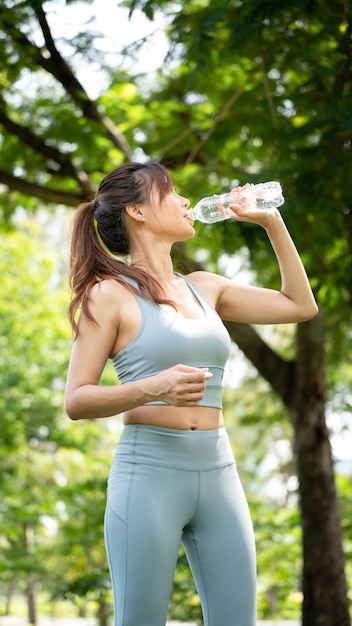 Femme de remise en forme eau potable jeune femme assoiffée buvant de l'eau d'une bouteille dans le parc d'été