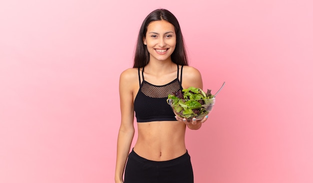 Femme de remise en forme hispanique semblant heureuse et agréablement surprise et tenant une salade