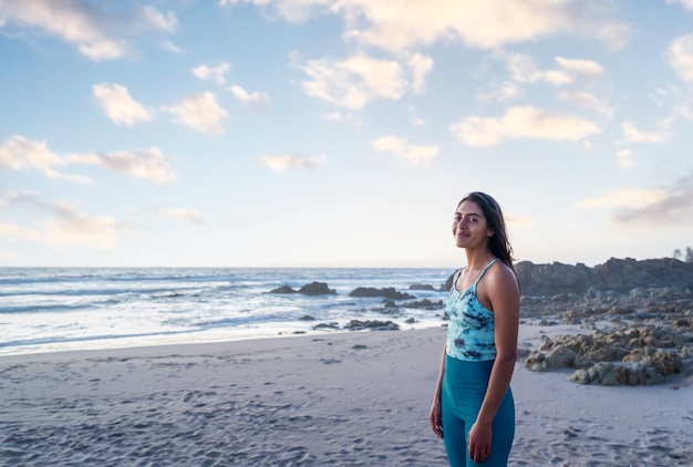 femme de remise en forme latine debout à la plage en regardant la caméra et souriant