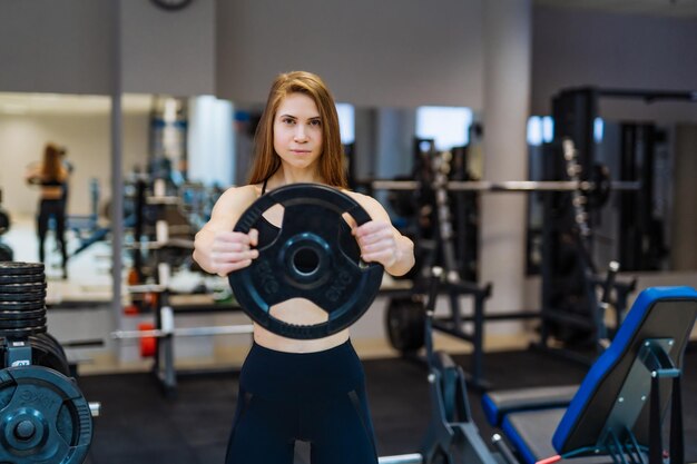 Femme de remise en forme séduisante en vêtements de sport posant avec un disque d'haltères à la salle de sport Femme de fitness sportive professionnelle avec disque de poids dans la salle de sport