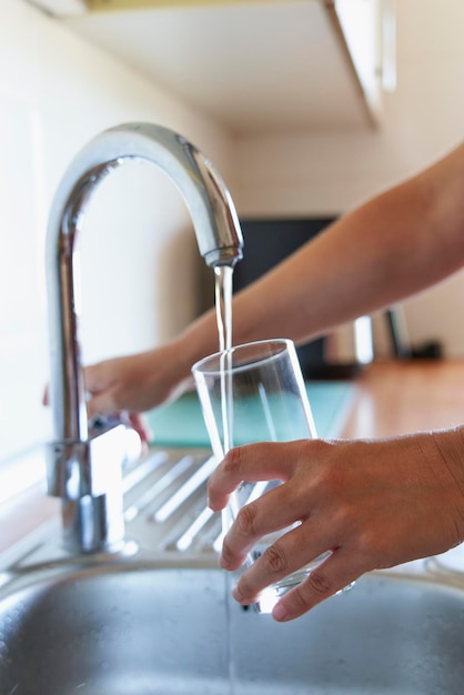 Une femme remplissant un verre d'eau fraîche au robinet de la cuisine