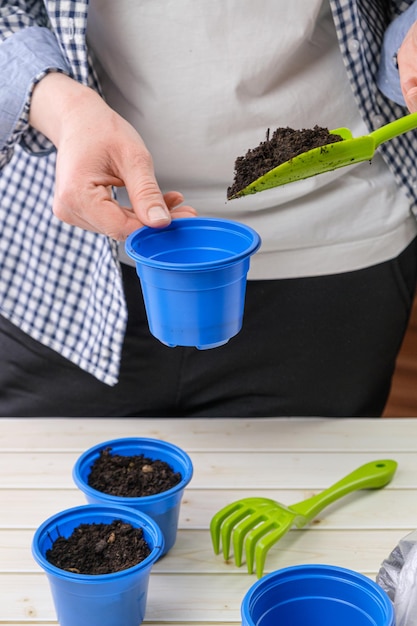 Femme remplit un petit pot de semis avec de la terre avec une pelle