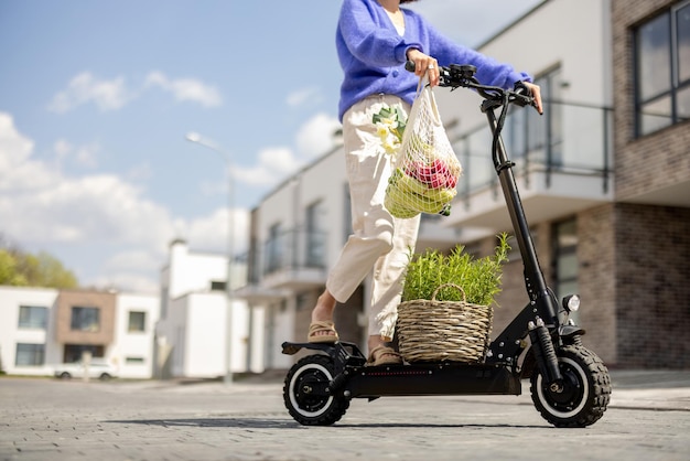 Femme rentrant à la maison avec des légumes frais sur un scooter électrique