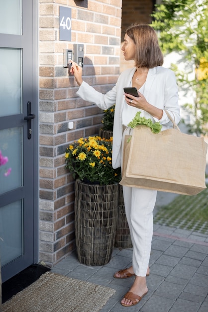 Une femme rentre à la maison avec des provisions et entre un code pour accéder à la porte