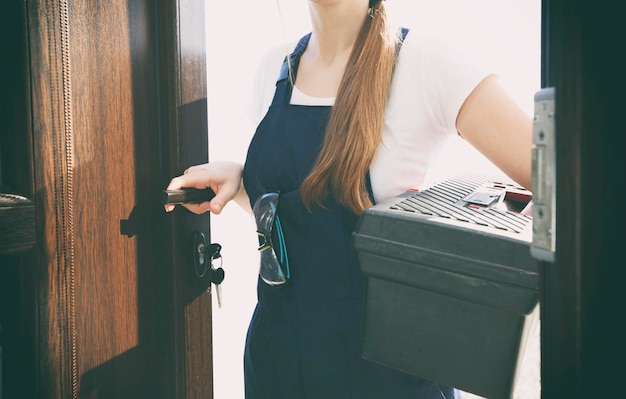 La femme réparatrice vêtue d'un uniforme de travail entre dans la maison avec une boîte à outils et d'autres équipements à la main