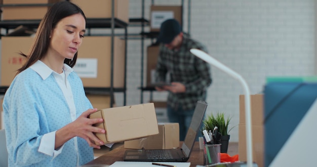 Une femme responsable du service d'assistance vérifie le numéro de commande sur le colis à l'aide d'un ordinateur prépare une boîte pour l'envoi Travail d'entrepôt