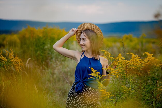 Femme restant sur le champ de fleurs sauvages à l'écart Copyspace. Souriante séduisante jeune fille brune portant des vêtements élégants et un chapeau rester sur la vallée des fleurs agricoles. Dame mignonne sur la place de la campagne.