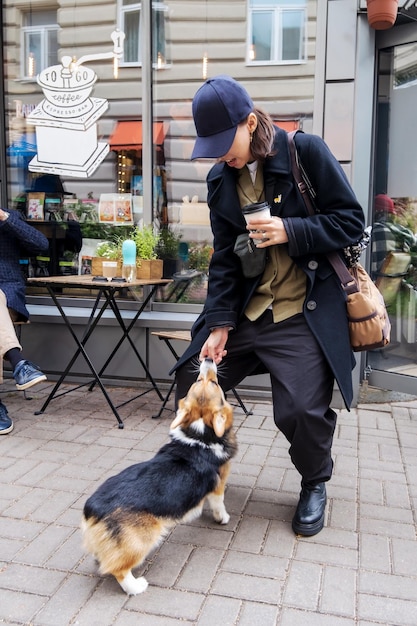 Une femme reste et joue avec un chien corgi sur une véranda extérieure à une table à casquette bleue