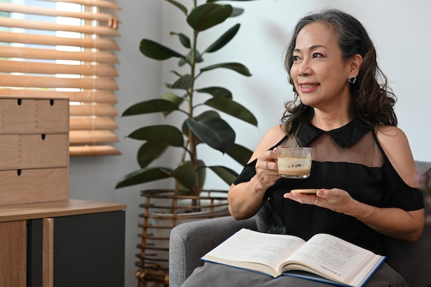 Une femme à la retraite satisfaite tenant une tasse de café et regardant par la fenêtre profite d'une humeur paisible sans stress