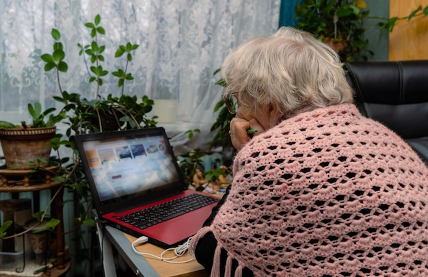 La femme retraitée lit des nouvelles à l'ordinateur portable à la maison