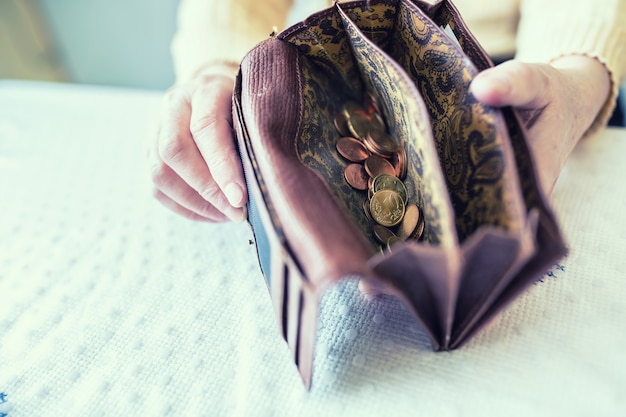 Femme retraitée tenant dans les mains un portefeuille avec des pièces en euros.