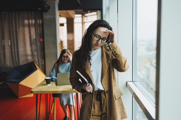 Une femme réussie à lunettes travaille au bureau sur le fond de collègues Journée de travail moderne au bureau Femme d'affaires prend des notes dans un cahier