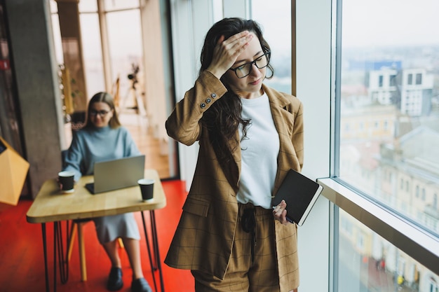 Une femme réussie à lunettes travaille au bureau sur le fond de collègues Journée de travail moderne au bureau Femme d'affaires prend des notes dans un cahier