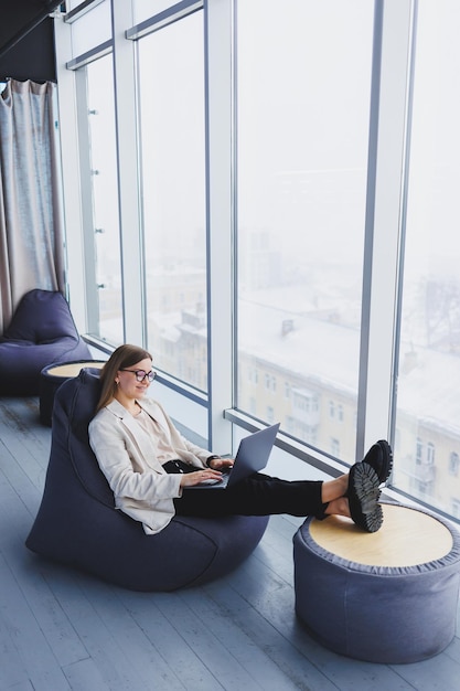 Une femme réussie en tenue décontractée tape sur un netbook tout en travaillant sur un nouveau projet tout en étant assise à un bureau dans un espace de travail moderne Femme d'affaires dans une veste et des lunettes Télétravail