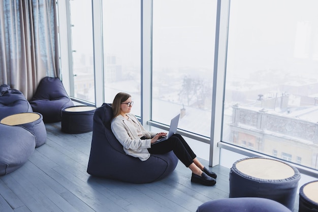 Une femme réussie en tenue décontractée tape sur un netbook tout en travaillant sur un nouveau projet tout en étant assise à un bureau dans un espace de travail moderne Femme d'affaires dans une veste et des lunettes Télétravail