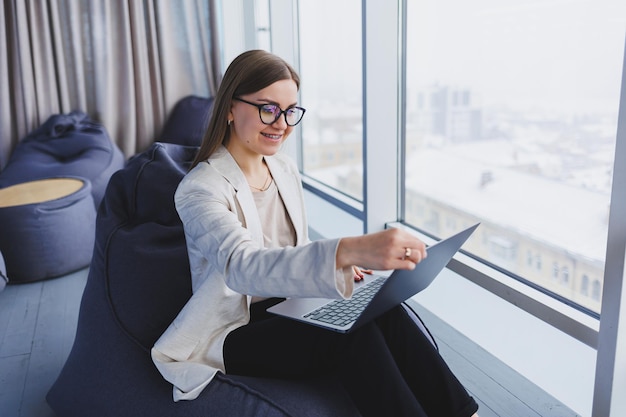 Une femme réussie en tenue décontractée tape sur un netbook tout en travaillant sur un nouveau projet tout en étant assise à un bureau dans un espace de travail moderne Femme d'affaires dans une veste et des lunettes Télétravail