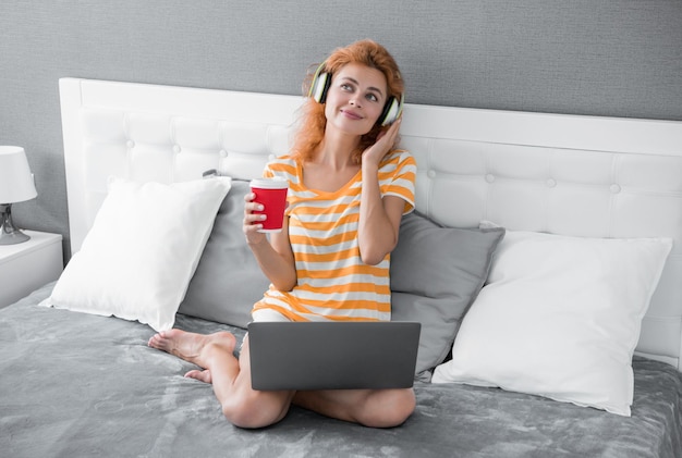 Femme rêveuse avec café écouter de la musique dans les écouteurs femme à la maison écouter de la musique