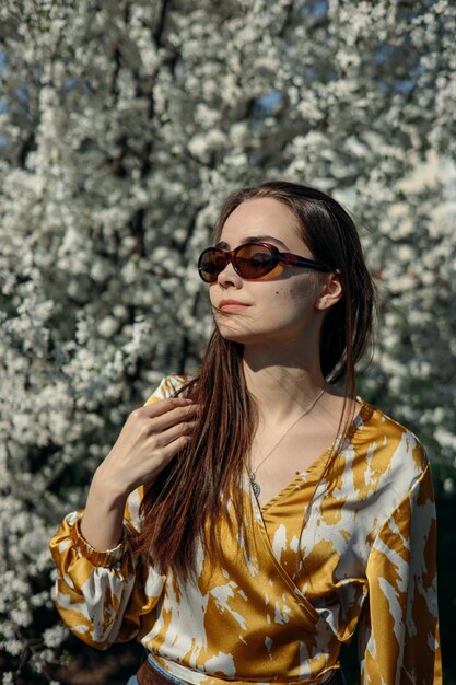 Femme rêveuse insouciante avec les yeux fermés touchant les cheveux dans le jardin de printemps avec des arbres en fleurs