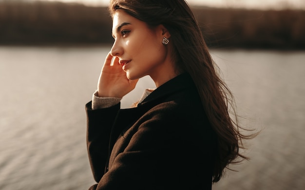 Femme rêveuse en manteau noir debout près de la rivière