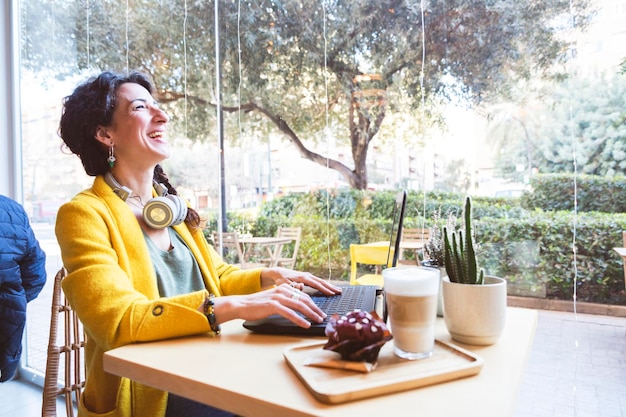 Femme riant devant un ordinateur portable dans une cafétéria