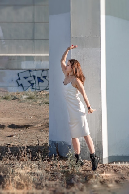 Femme en robe blanche et aux cheveux longs posant sous le pont sur fond de béton