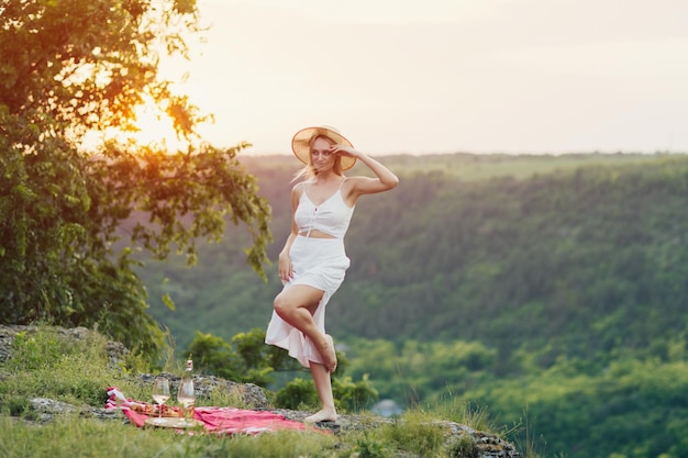femme en robe blanche et chapeau de paille dans la montagne lors d'un pique-nique d'été