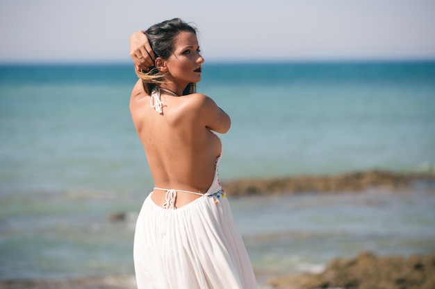 Femme en robe blanche et dos à l'air debout sur la plage