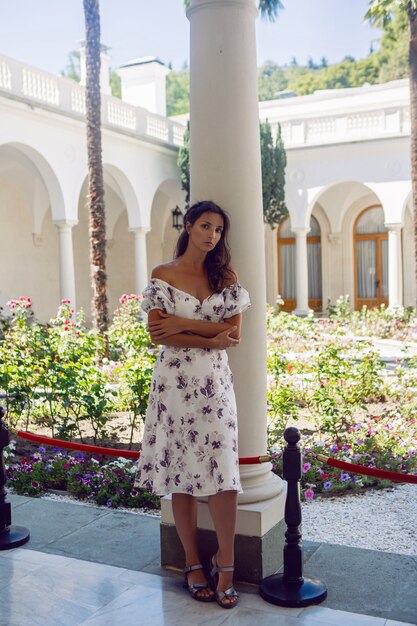 Femme en robe blanche avec des fleurs se tient à l'entrée de la porte du château avec des colonnes