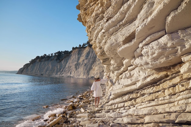 Femme en robe blanche marchant près du rivage au bord de la falaise