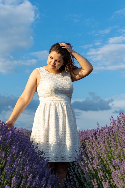 Une femme en robe blanche marche parmi les rangées de lavande.