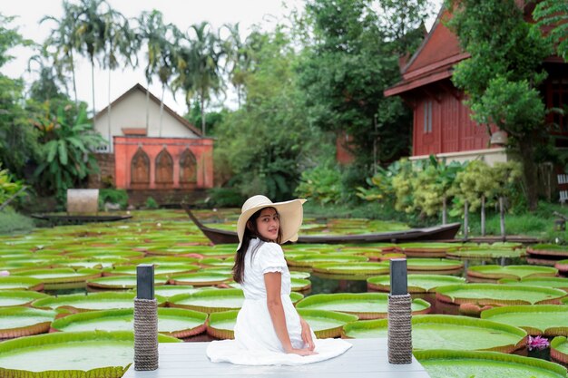 Femme en robe blanche s'asseoir sur le pont au-dessus de la piscine avec une grande feuille de lotus victoria verte