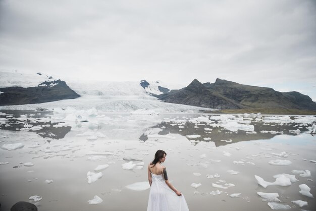 Femme en robe blanche se dresse sur fond de glaciers en Islande