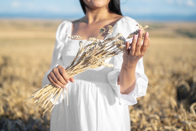 Une femme en robe blanche se tient dans un champ avec une personne de blé tenant dans les mains un paquet d'épillets mûrs moisson...