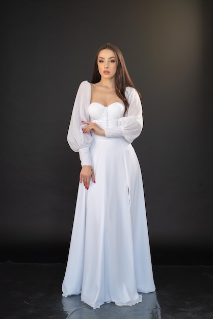 Une femme en robe blanche se tient devant un fond noir.