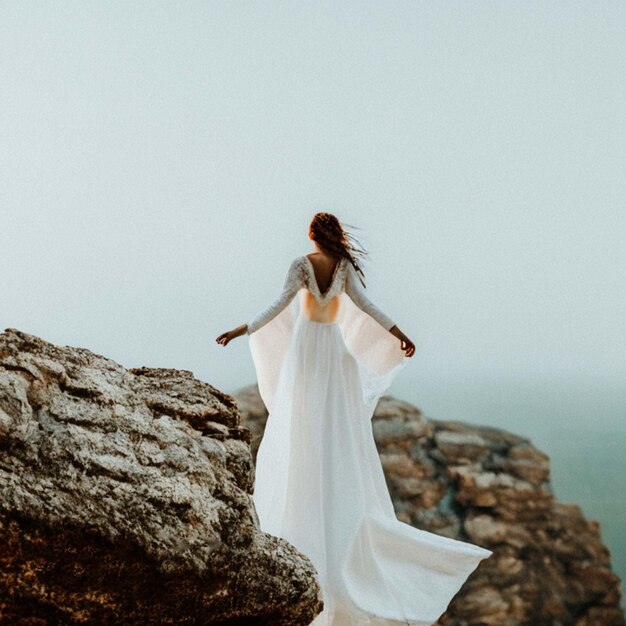 Photo une femme en robe blanche se tient sur une falaise avec l'océan en arrière-plan