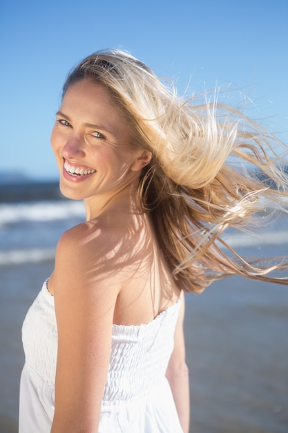 Femme en robe blanche, souriant à la caméra sur la plage