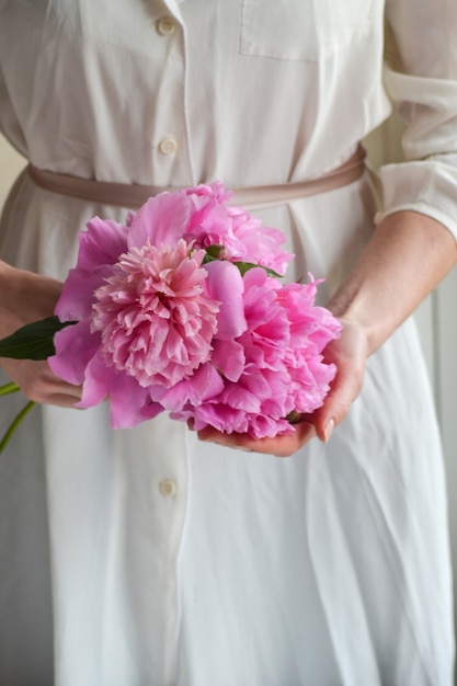 Femme en robe blanche tenant des fleurs de pivoines pions roses. Fermer