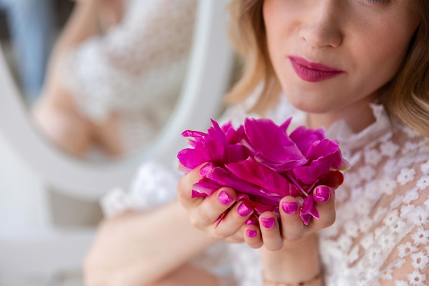 Femme en robe blanche tenant des pétales de pivoine rose dans ses mains Fête des mères ou Saint Valentin