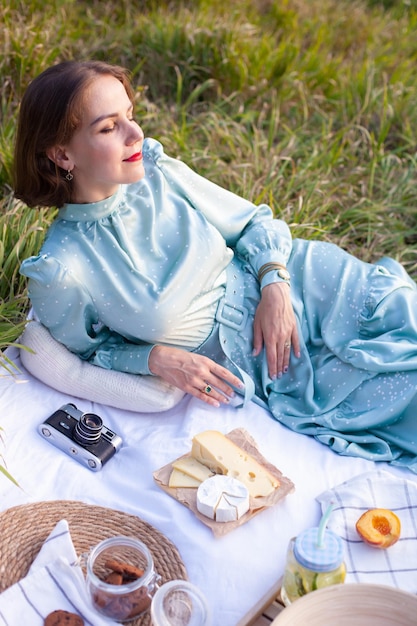 Une femme en robe bleue est assise sur un pique-nique dans un parc avec vue panoramique