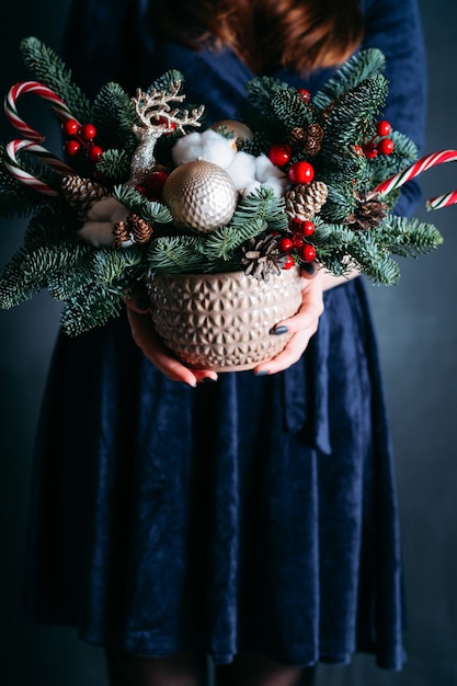 femme en robe bleue tenant un pot avec sapin, cerf, cannes de bonbon.