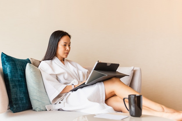 Femme en robe de chambre s'asseoir sur le canapé travaillant sur un ordinateur portable