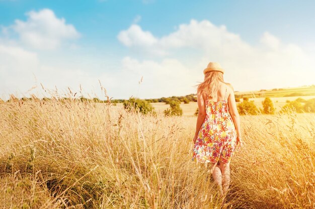 Femme en robe et chapeau marchant dans un champ de blé en été