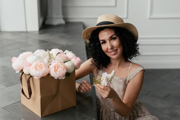 Femme en robe et chapeau de paille à côté de bouquet de fleurs blanc et rose