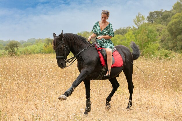 Femme en robe avec un cheval noir dans la nature