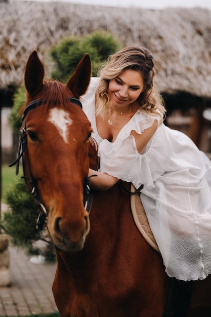 Une femme en robe d'été blanche à cheval près d'une ferme