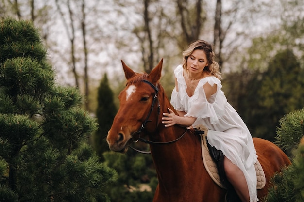 Une femme en robe d'été blanche à cheval près d'une ferme